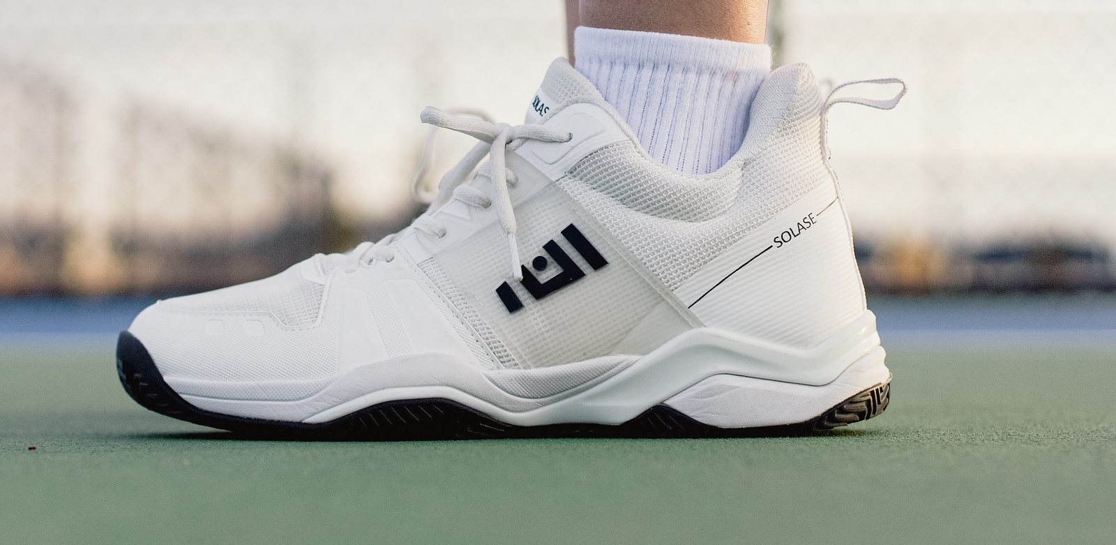 Close-up of a white Solase pickleball shoe on a green court